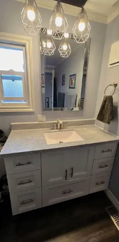 Bathroom vanity after the update: a light top, undermount sink, new faucet and frameless mirror on the original cabinets